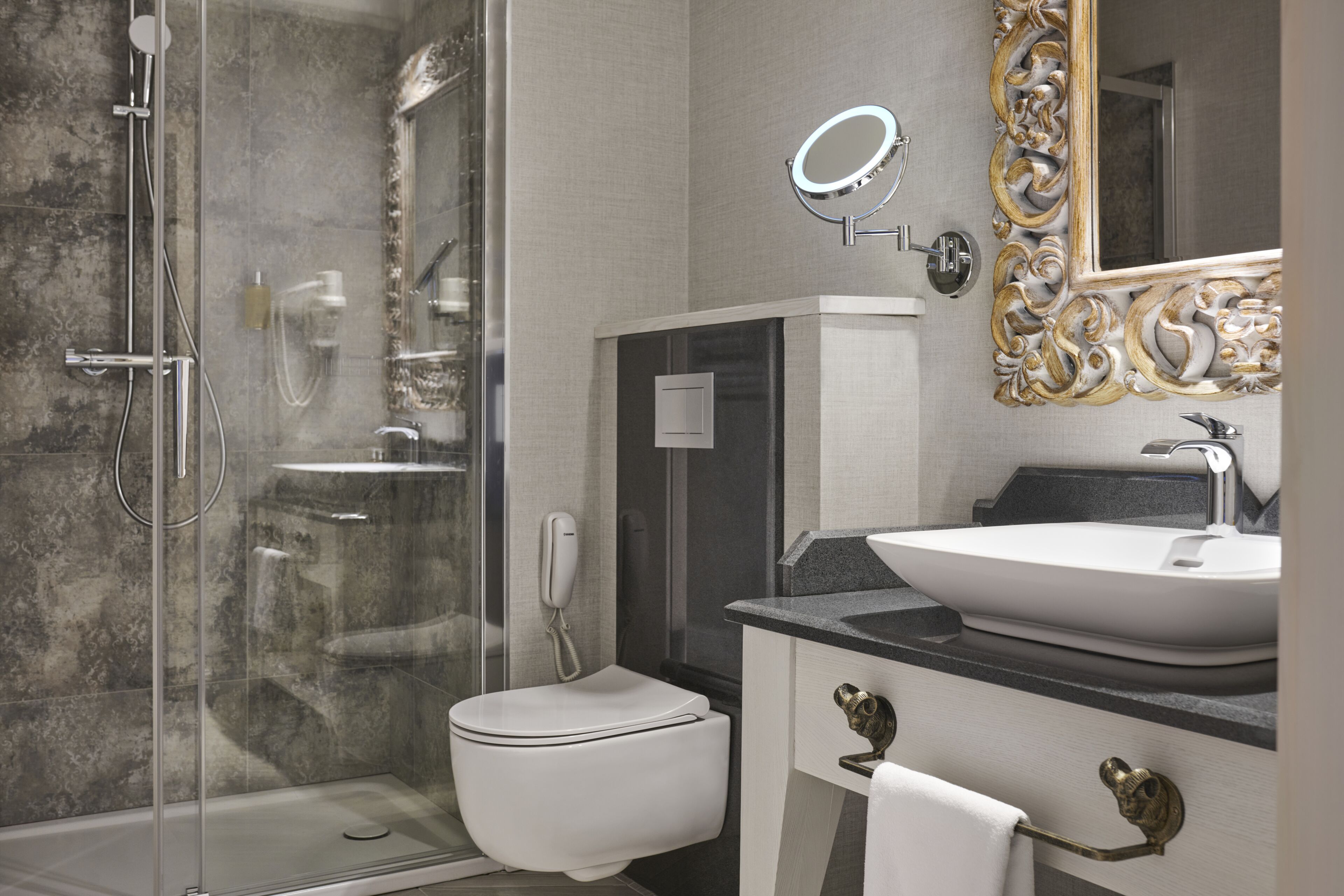 A modern bathroom with a glass-enclosed shower, a white toilet, a vanity with a large sink, and a decorative mirror.
