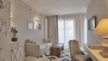A modern hotel room with a sofa, armchair, and a desk with a lamp.