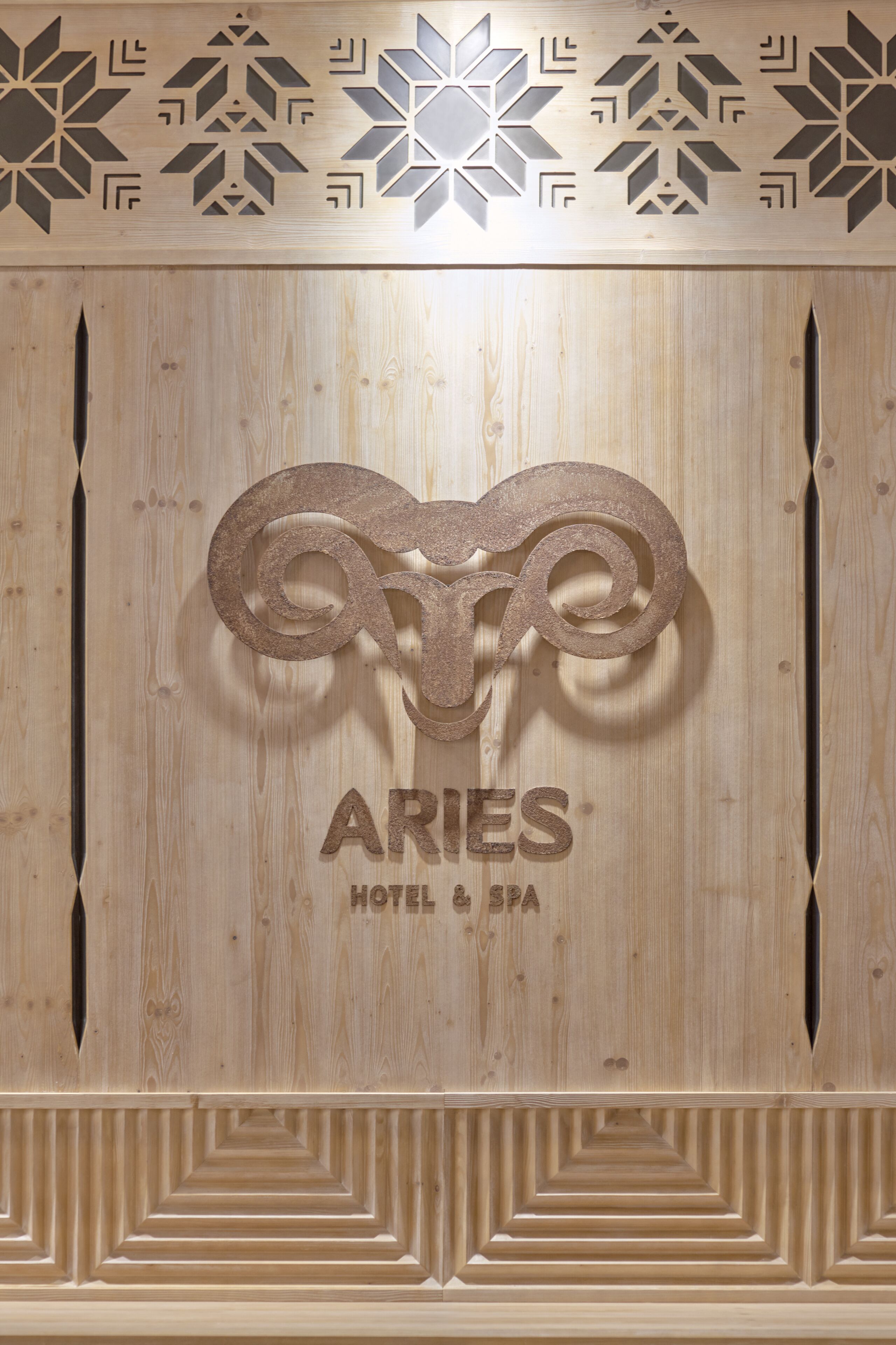 Un panel de madera con un diseño geométrico y el texto "ARIES HOTEL & SPA".