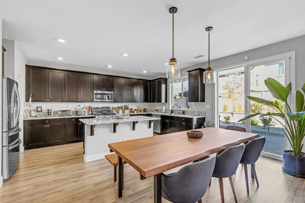 Une cuisine moderne avec des meubles de couleur sombre, un îlot central et un coin repas comprenant une table et des chaises en bois.