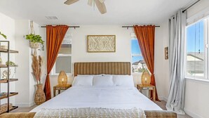 A bedroom with a large bed, two bedside tables with lamps, a ceiling fan, and a view of the outside. - New South Reno Home with Hot Tub (Reno)