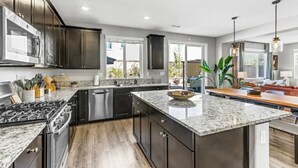 A modern kitchen with dark cabinets, a granite countertop, stainless steel appliances, and a large island. - New South Reno Home with Hot Tub (Reno)