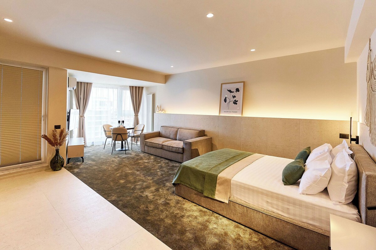 A hotel room with a bed, a sofa, a dining table, and a chair.