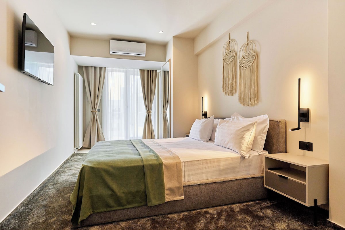 A hotel room with a bed, a bedside table, a TV mounted on the wall, and a wall-mounted air conditioner.