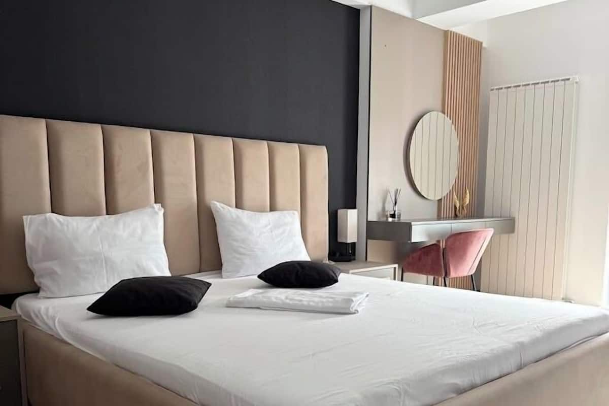 A modern bedroom with a large bed, a bedside table, a chair, and a mirror.