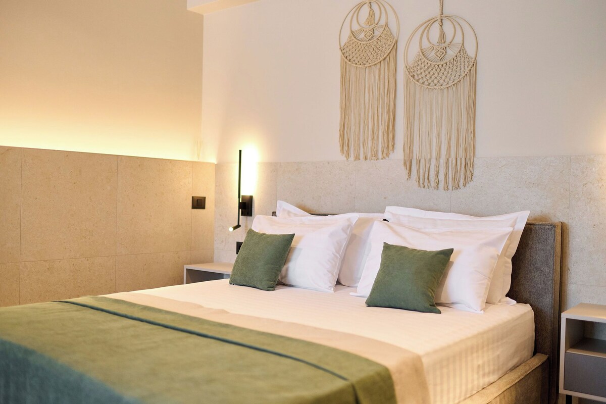 A neatly made bed with white and green pillows, a green throw blanket, and a macrame wall hanging.