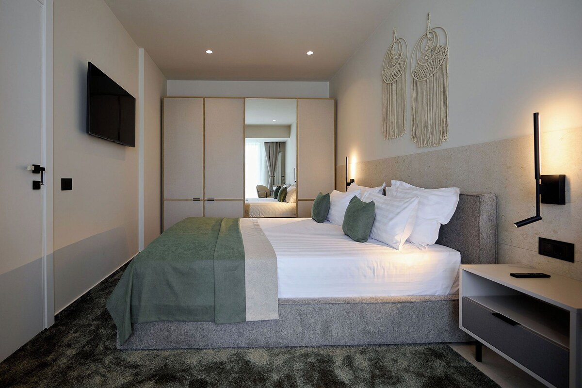 A modern hotel room with a large bed, a bedside table, a TV mounted on the wall, and a wardrobe with sliding doors.