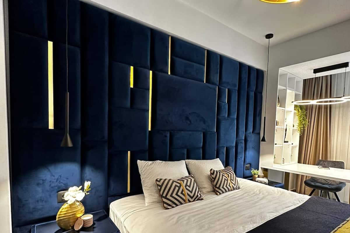 A modern bedroom with a tufted headboard, bedside tables, a bed with patterned pillows, and a hanging light fixture.