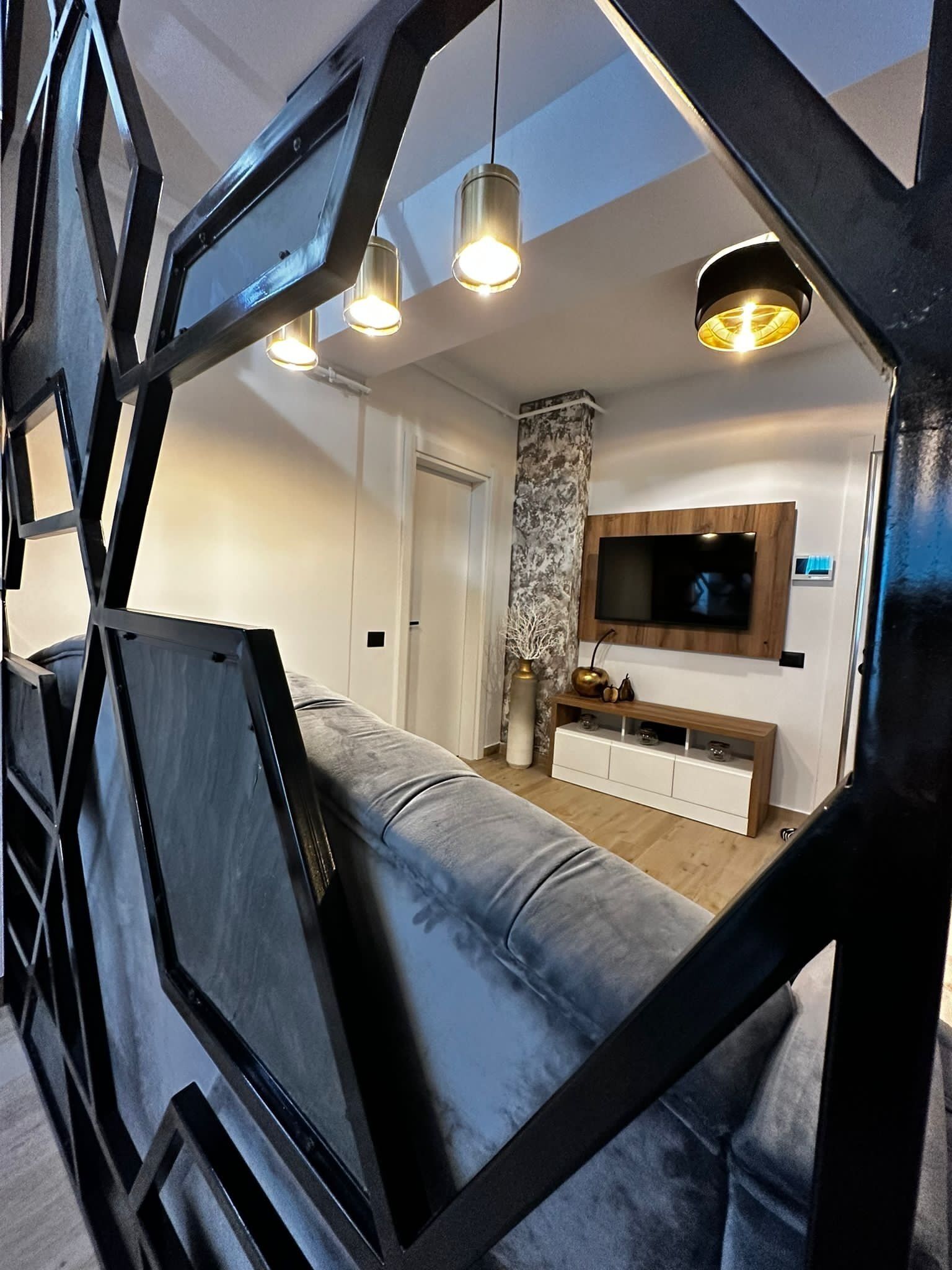 A modern living room with a grey sofa, a TV mounted on the wall, and pendant lights.