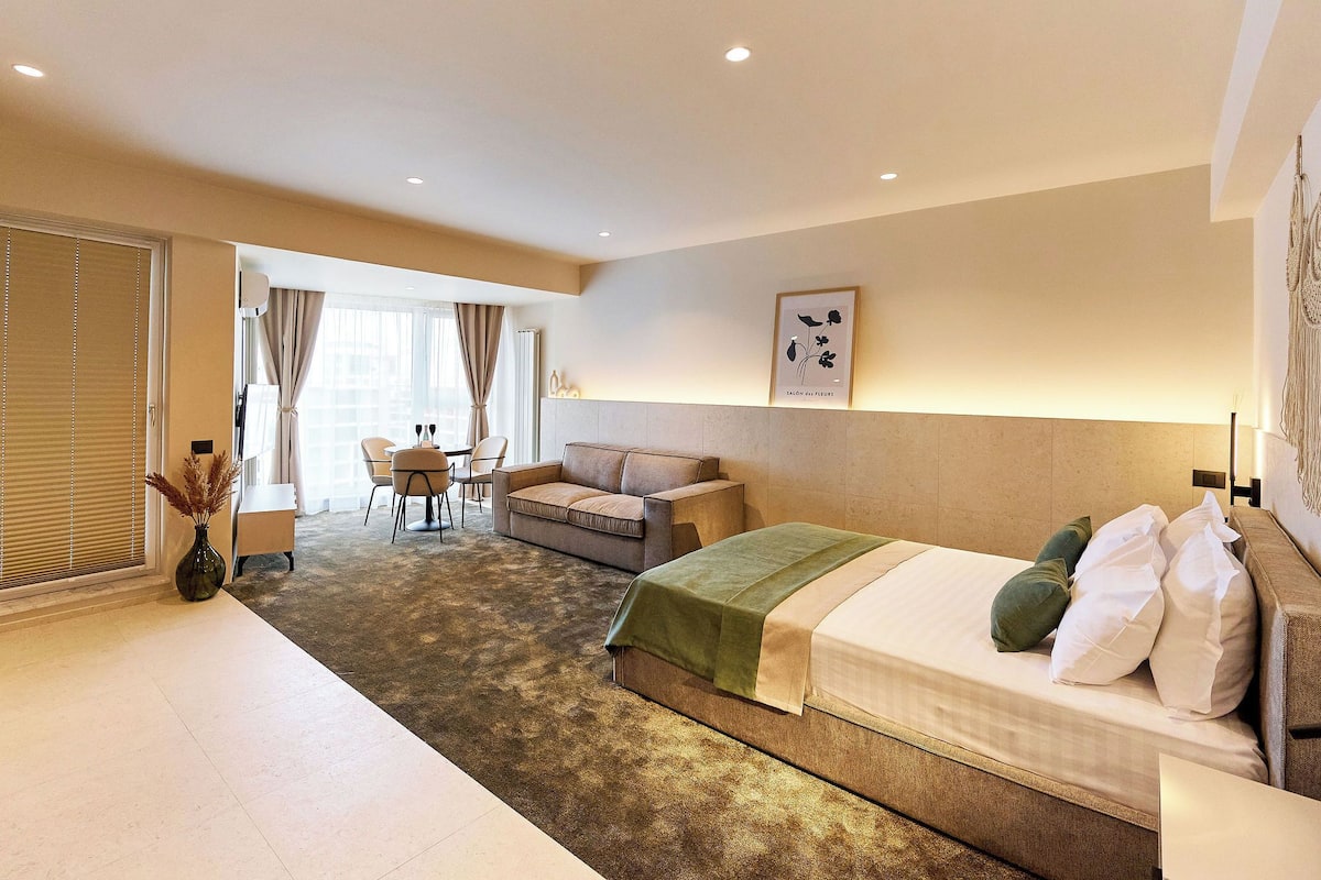 A hotel room with a bed, a sofa, a dining table, and a chair.