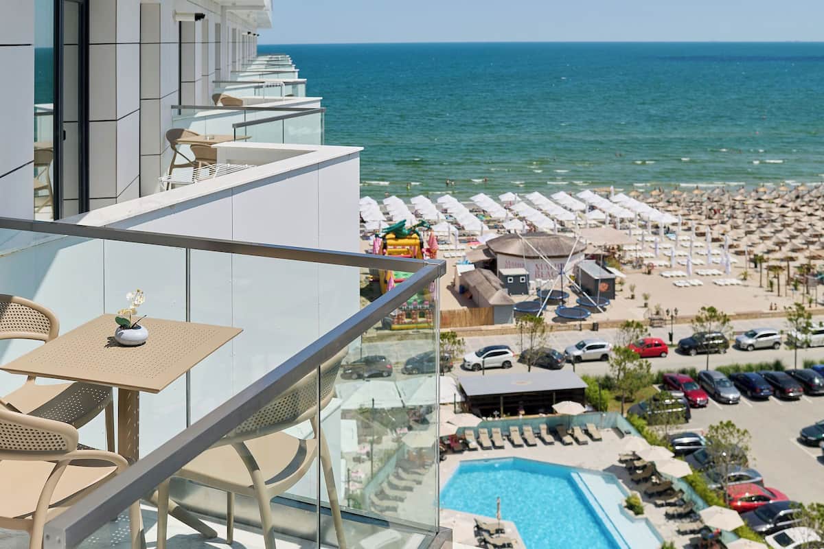 A balcony with a view of a beach resort, including a pool and sun loungers.