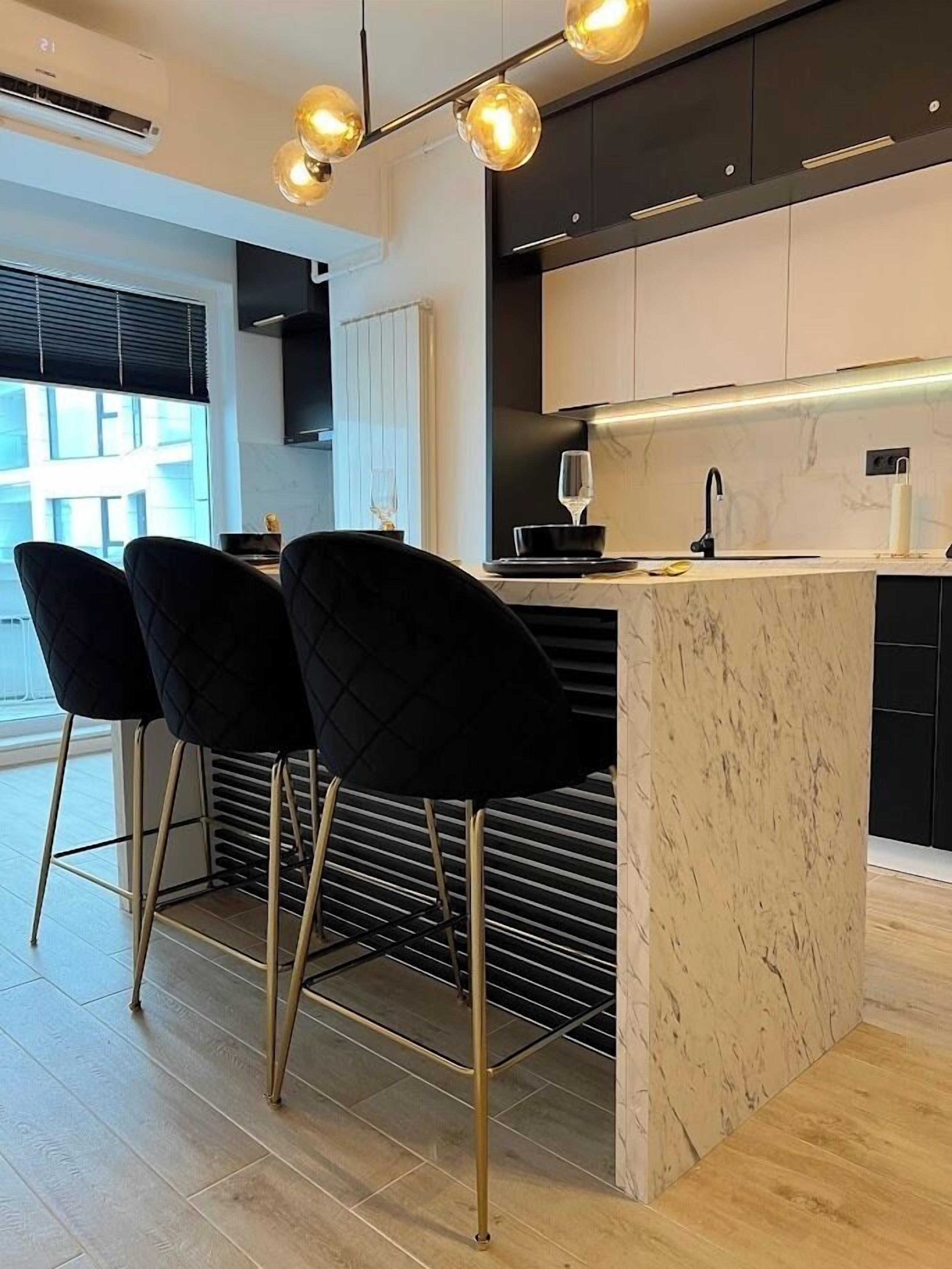 Een moderne keuken met een marmeren kookeiland, zwarte stoelen en hanglampen.