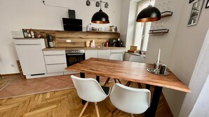A modern kitchen with a wooden table and two white chairs, a built-in oven, and a black range hood. - Firstclass 2r_apartment (Leipzig)
