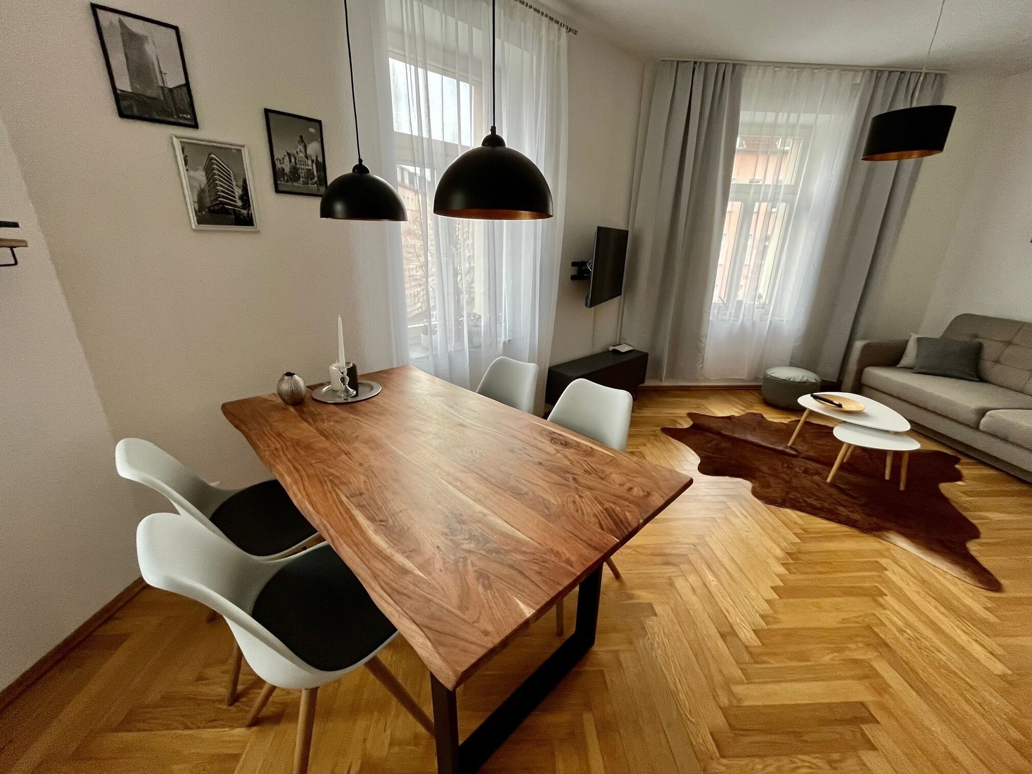 Ein modernes Wohnzimmer mit einem Holzesstisch, weißen Stühlen, einer Couch und einem Lederteppich.