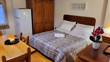 A bedroom with a bed, wooden wardrobe, a small table with candles, and a potted plant.