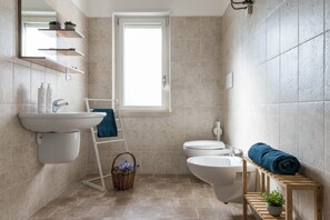 Un baño moderno con lavamanos, inodoro, bidé, una ventana y un perchero para toallas.