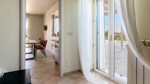 Habitación de hotel con puerta corrediza de vidrio que da a un área exterior, una mesa de comedor con sillas y una pequeña cocina.