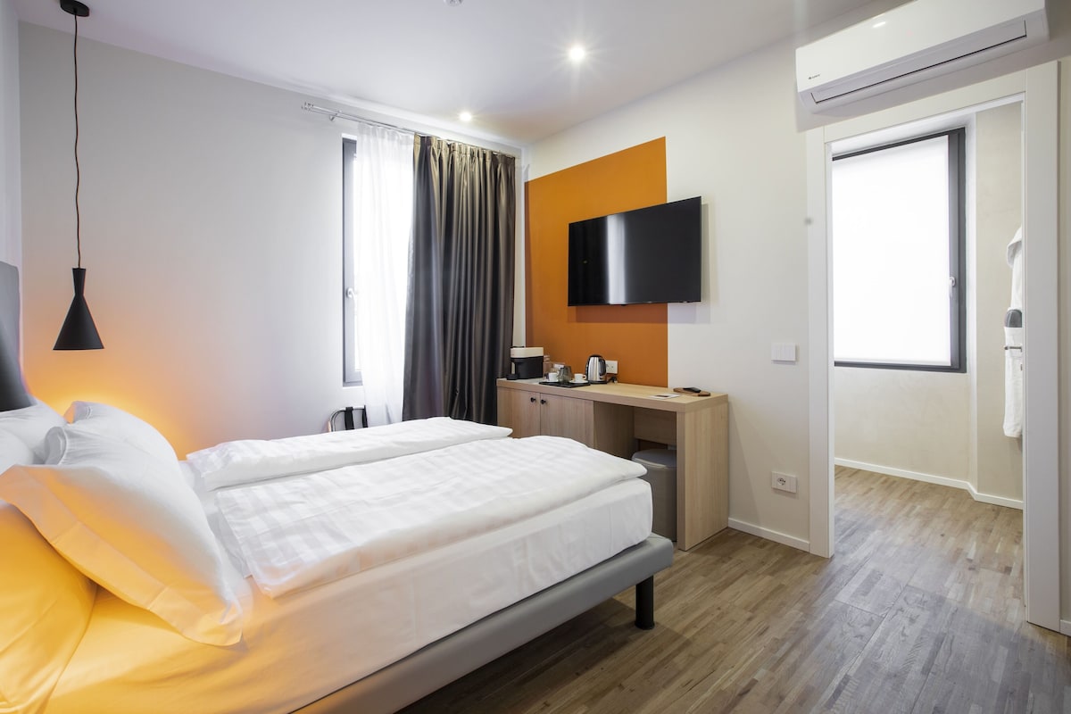 Una habitación de hotel con cama, escritorio, televisión y aire acondicionado.