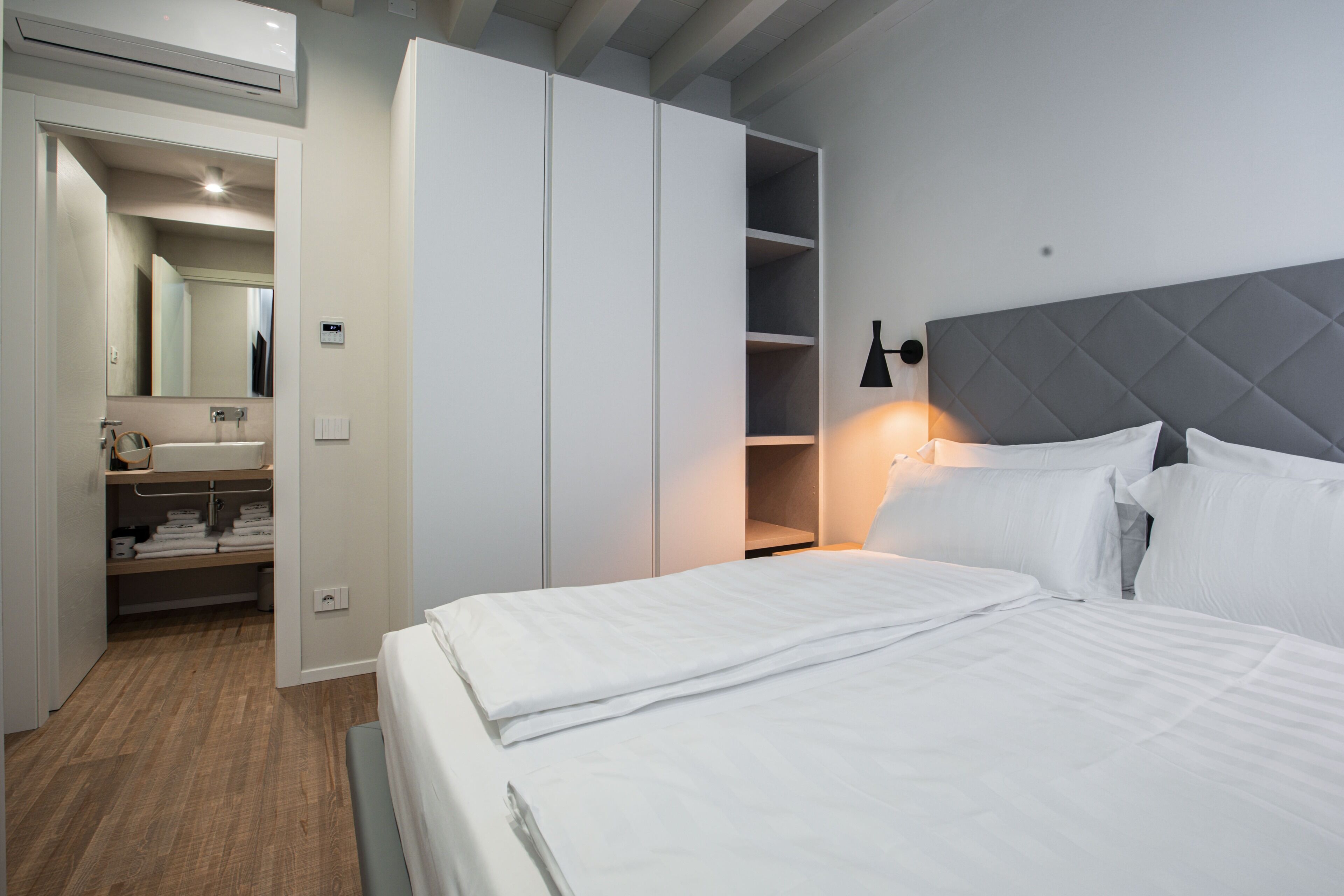Een moderne hotelkamer met een groot bed, een kledingkast, een kaptafel met spiegel en een bedlampje.