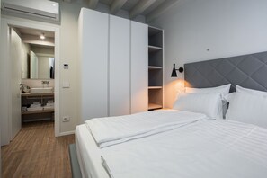 Une chambre d’hôtel moderne avec un grand lit, une armoire, une coiffeuse avec un miroir et une lampe de chevet.