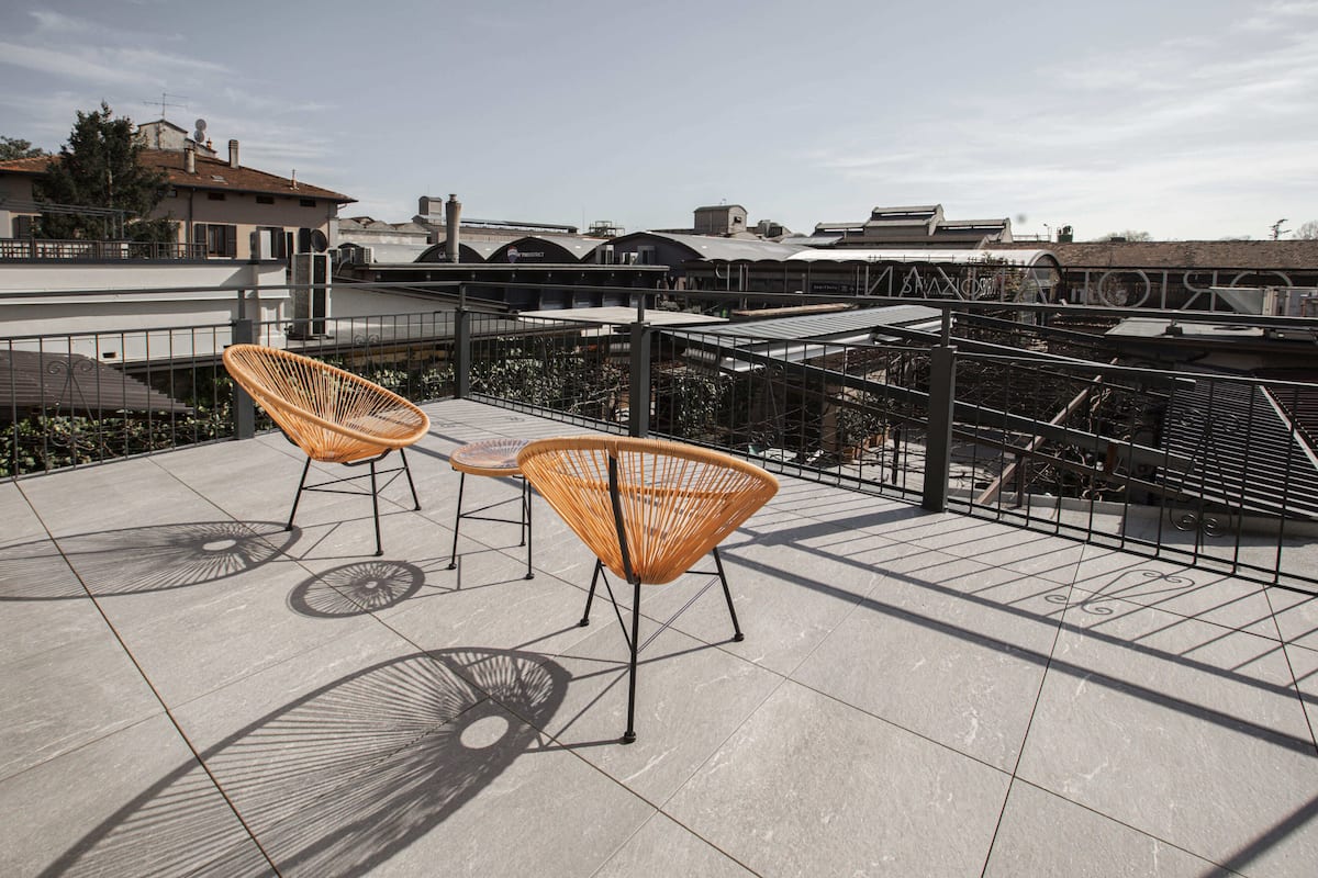 Una terraza en la azotea con dos sillones de mimbre, una baranda de metal y vistas a edificios al fondo.