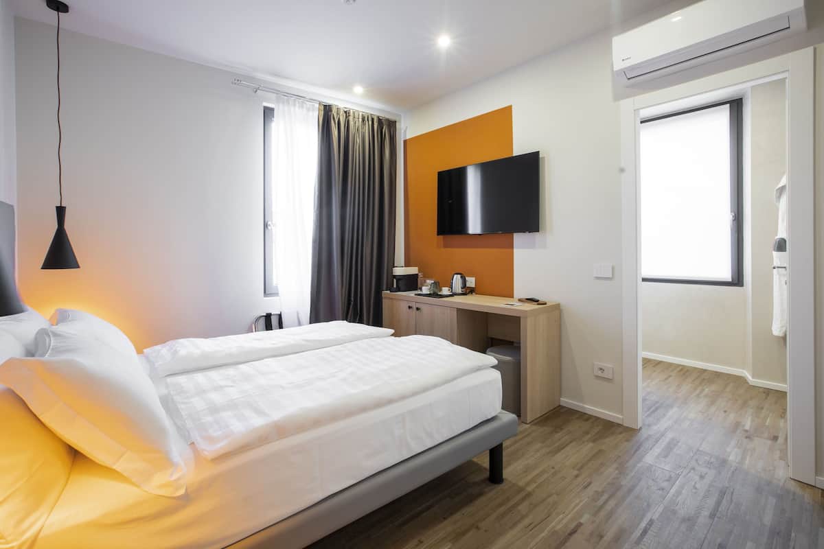 Una habitación de hotel moderna con una cama grande, un escritorio, un televisor de pantalla plana y un equipo de aire acondicionado.