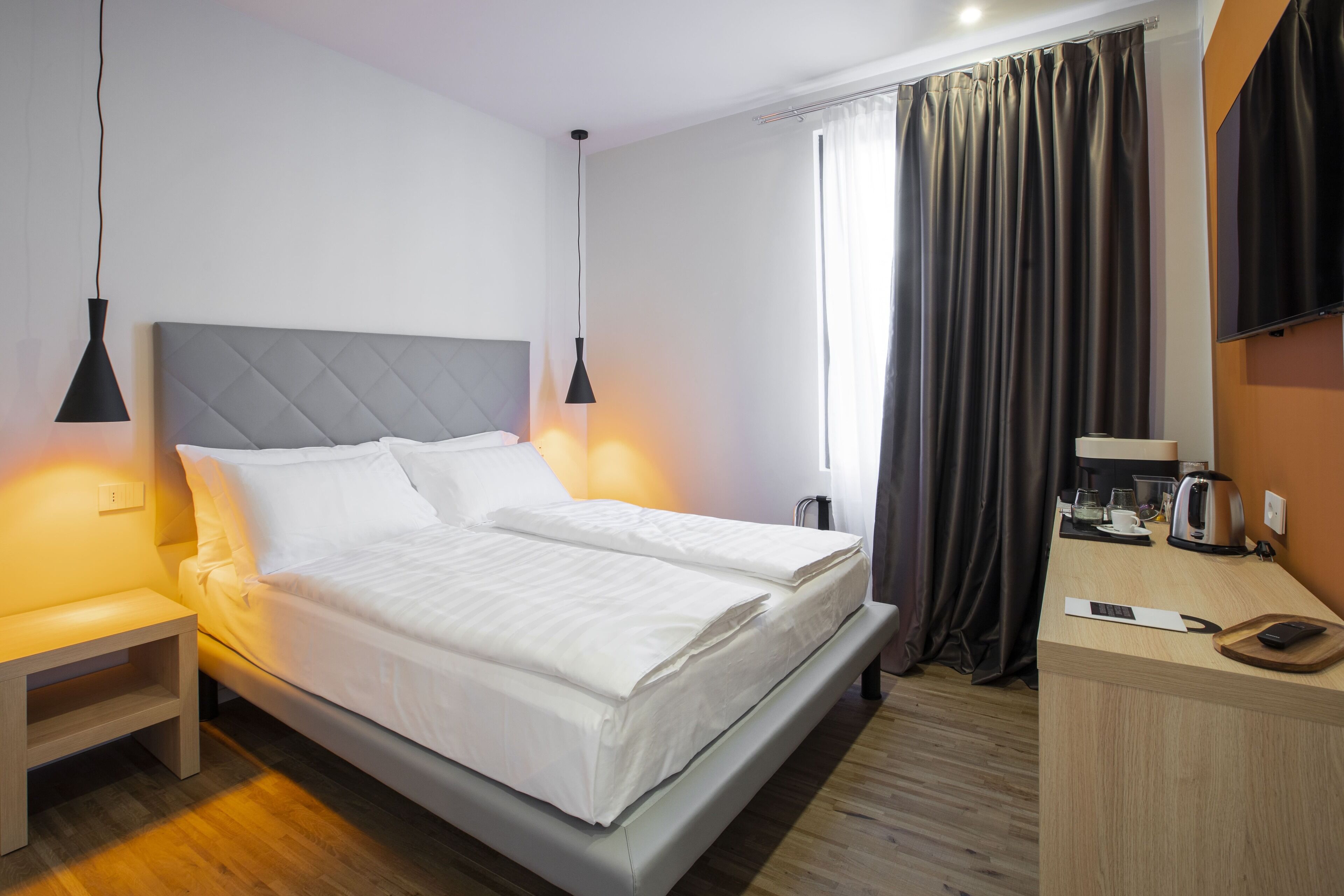 Ein Hotelzimmer mit Bett, Nachttisch und Schreibtisch, inklusive Wasserkocher und Kaffeemaschine.