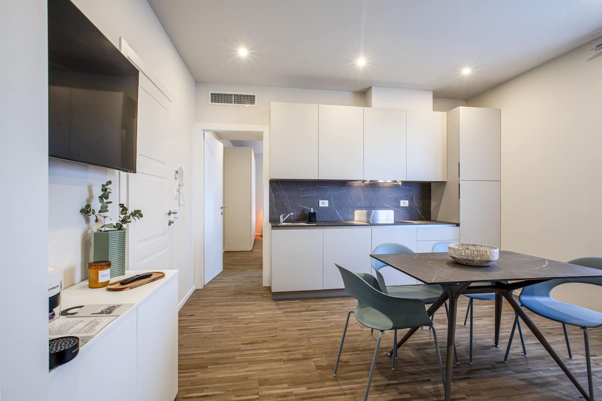 Una cocina moderna con armarios blancos, una encimera de mármol y un comedor con mesa y sillas.