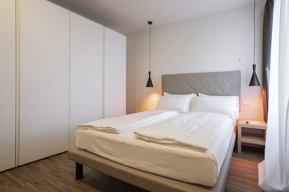Una cama bien hecha con cabecera, mesitas de noche y una lámpara colgante.