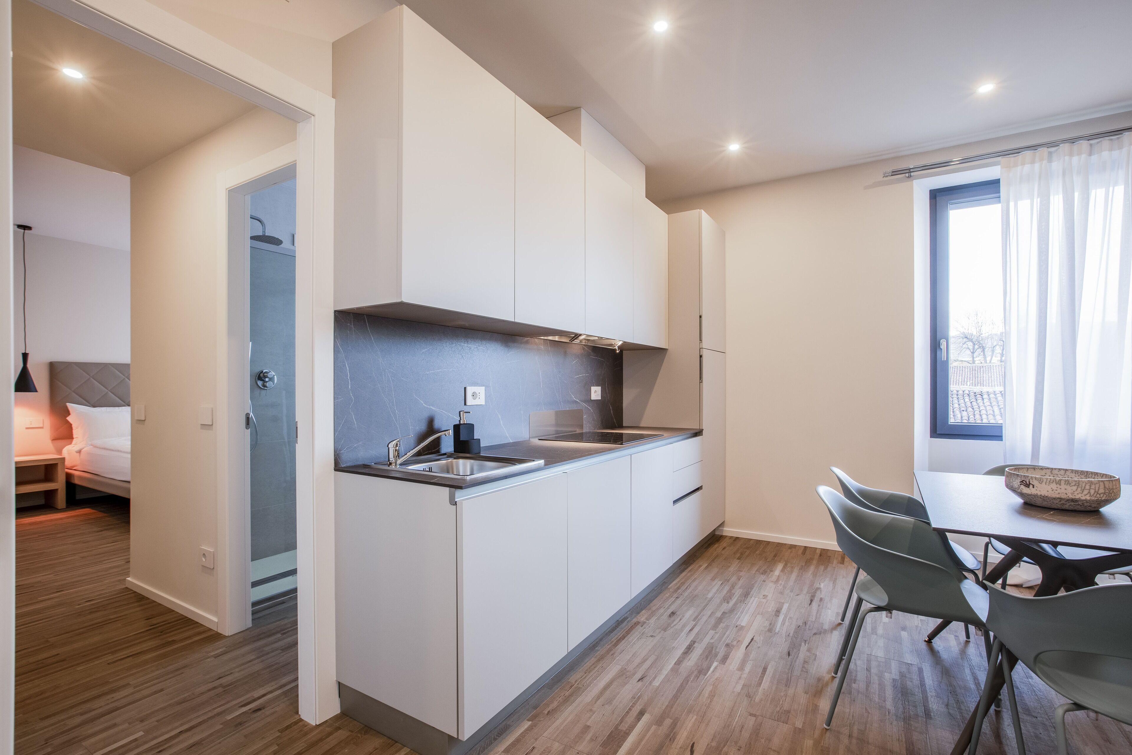 A modern kitchen with white cabinets, a built-in oven, and a dining area with a table and chairs.