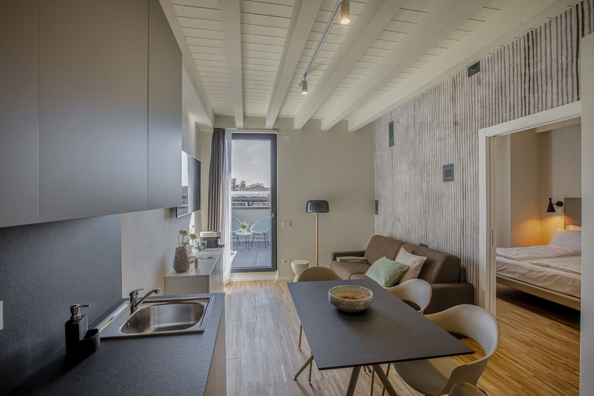 Una habitación de hotel compacta con kitchenette, zona de comedor, sofá y cama.