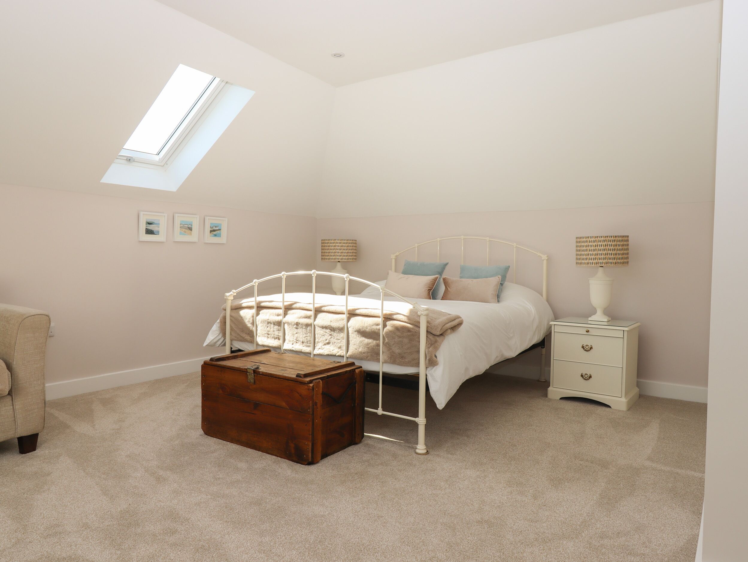 A bedroom with a skylight, a bed with pillows, a bedside table with a lamp, a chest of drawers, and a suitcase.