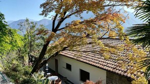 Un edificio tradizionale con tetto in tegole, immerso nel verde e con montagne sullo sfondo.