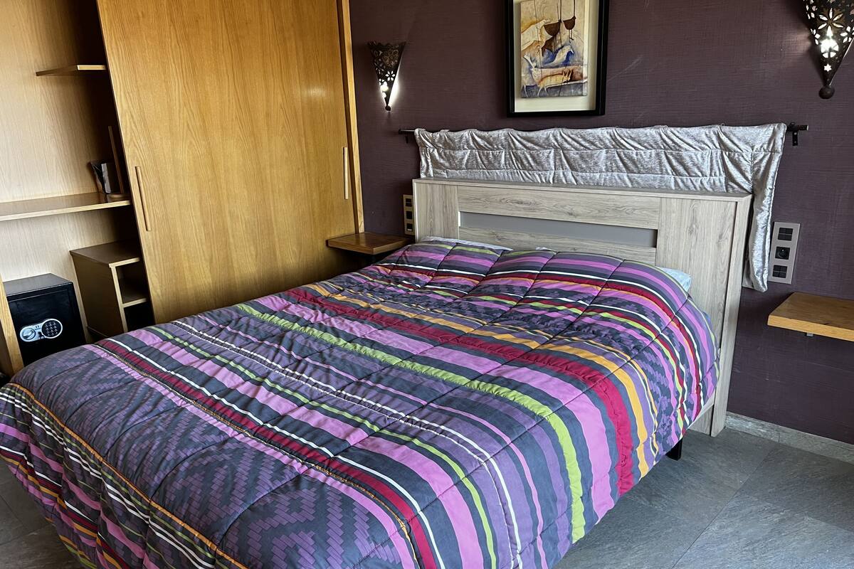 A bedroom with a bed, wooden wardrobe, bedside tables, and a wall-mounted light fixture.