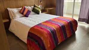 A hotel room with a large bed, a wooden headboard, a nightstand, and a view of the outside through a sliding door.
