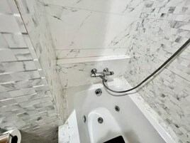 Eine Badewanne mit Duschkopf und Ablauf, umgeben von weißen Marmorfliesen.