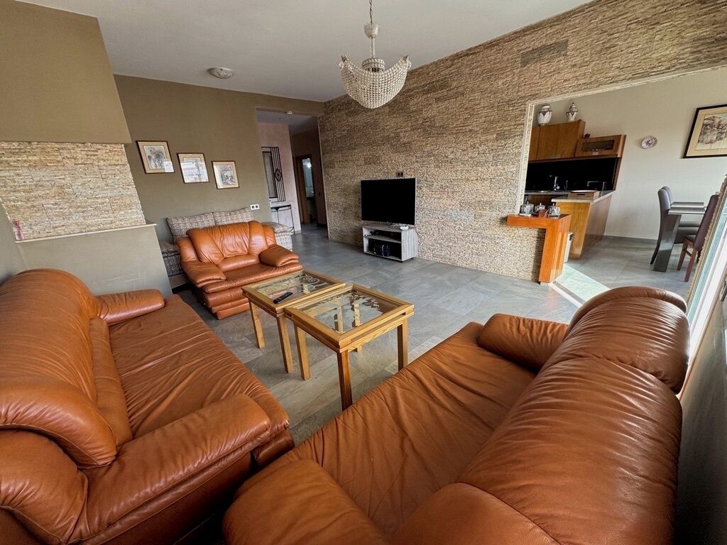 A living room with leather sofas, a coffee table, a TV, and a kitchen area with a counter and chairs.