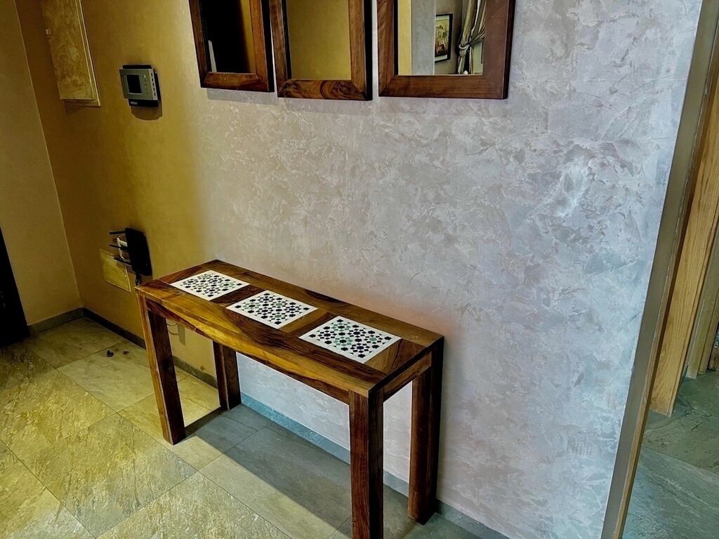 Una panca di legno con motivo a scacchiera, un termostato a parete e uno specchio.