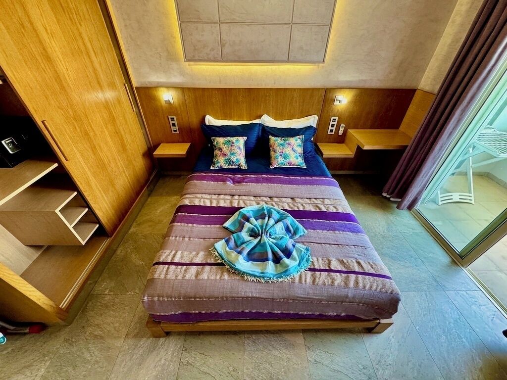 Een hotelkamer met een bed, nachtkastjes, een houten kledingkast en een glazen deur naar een balkon.