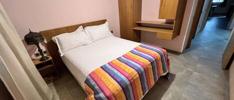 A neatly made bed with a colorful striped bedspread, a bedside lamp, and a wooden headboard.