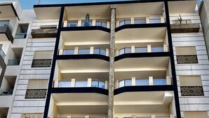 A multi-story building with a modern architectural design, featuring balconies, a central entrance with a glass door, and a sign indicating it is a residence.
