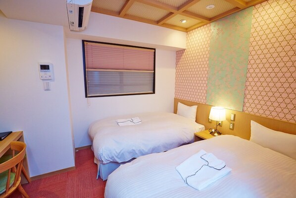 Two single beds, a desk, and air conditioning unit are featured in this well-maintained room.