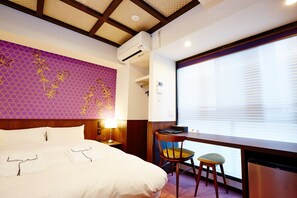 Relax in a stylish room with a large bed, desk, and window with blinds.
