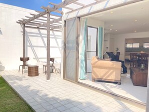 Une terrasse extérieure moderne, dotée d’une pergola, d’un canapé et d’un coin repas, visible à travers une porte vitrée.