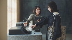 Una reception con una postazione self-service digitale, una persona che indica lo schermo e un'altra in piedi accanto.