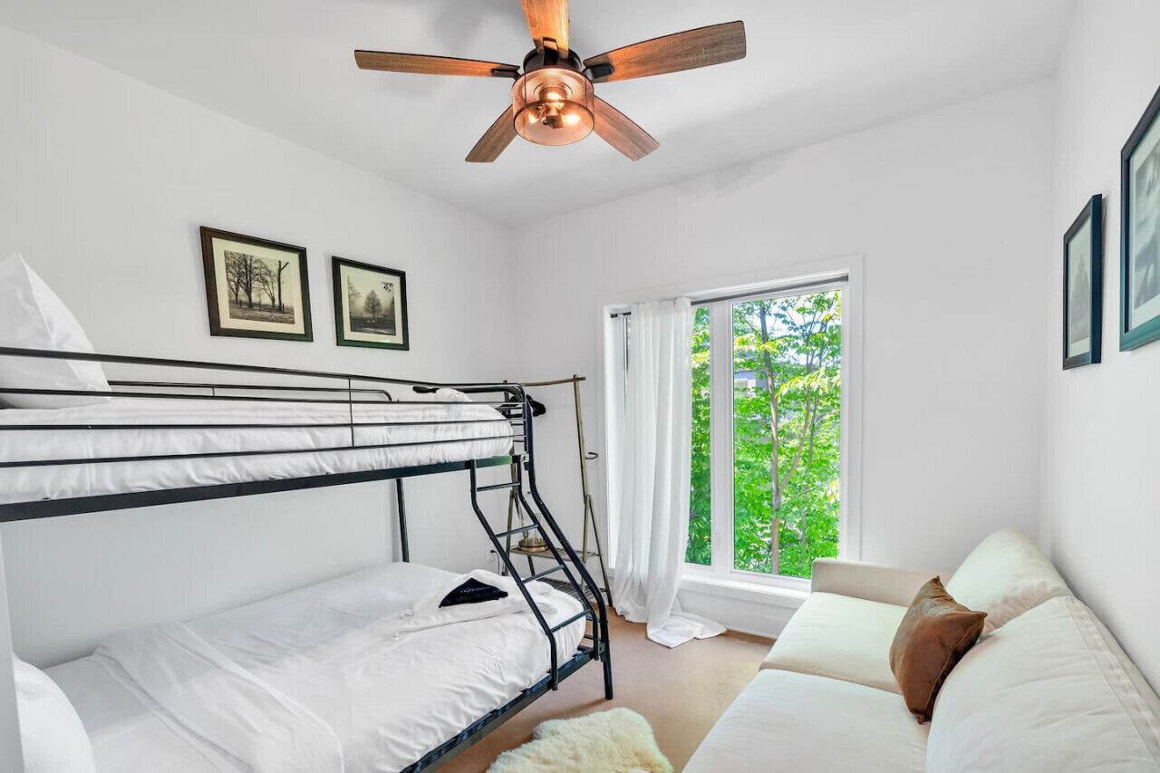 A room with bunk beds, a ceiling fan, a window with curtains, and a sofa.