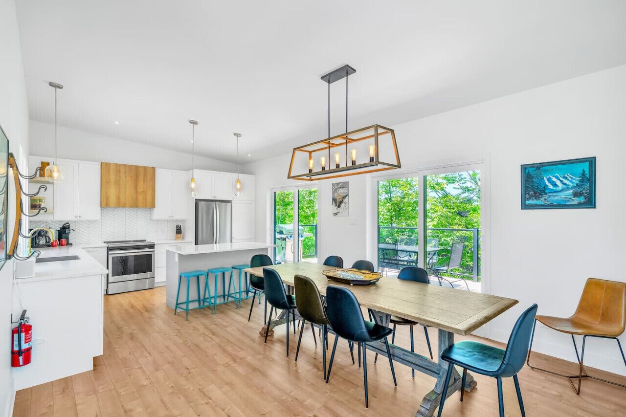 Una cocina moderna con armarios blancos, una isla de madera y una zona de comedor con una mesa grande y sillas.