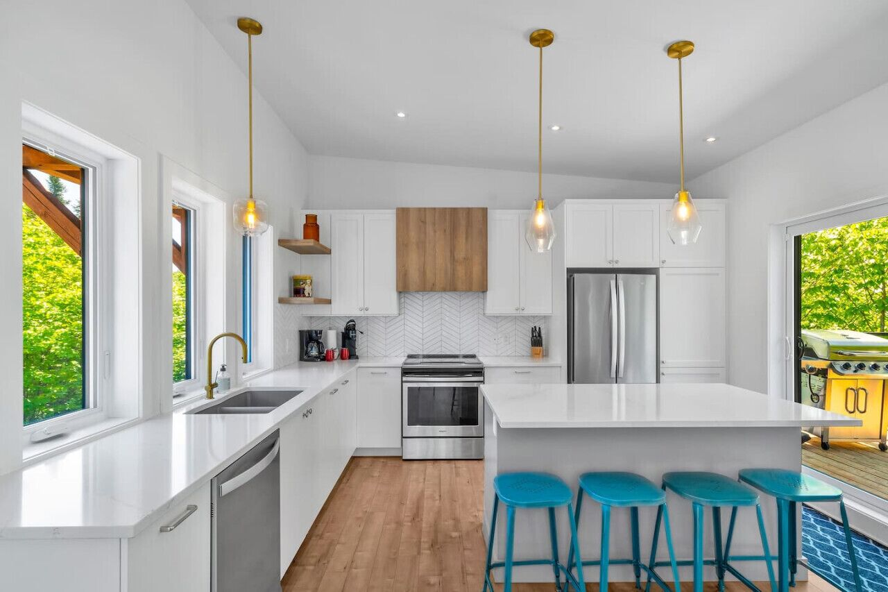 A modern kitchen with white cabinetry, a central island with bar stools, stainless steel appliances, and pendant lighting.