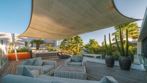 Un espacio lounge exterior moderno con mobiliario de mimbre, una parrilla y plantas en macetas.