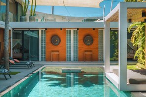 Un área de piscina moderna con piscina cristalina, sillones de descanso y una sala acristalada con vistas.